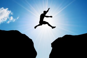 Man jumping over precipice between two rocky mountains at sun li
